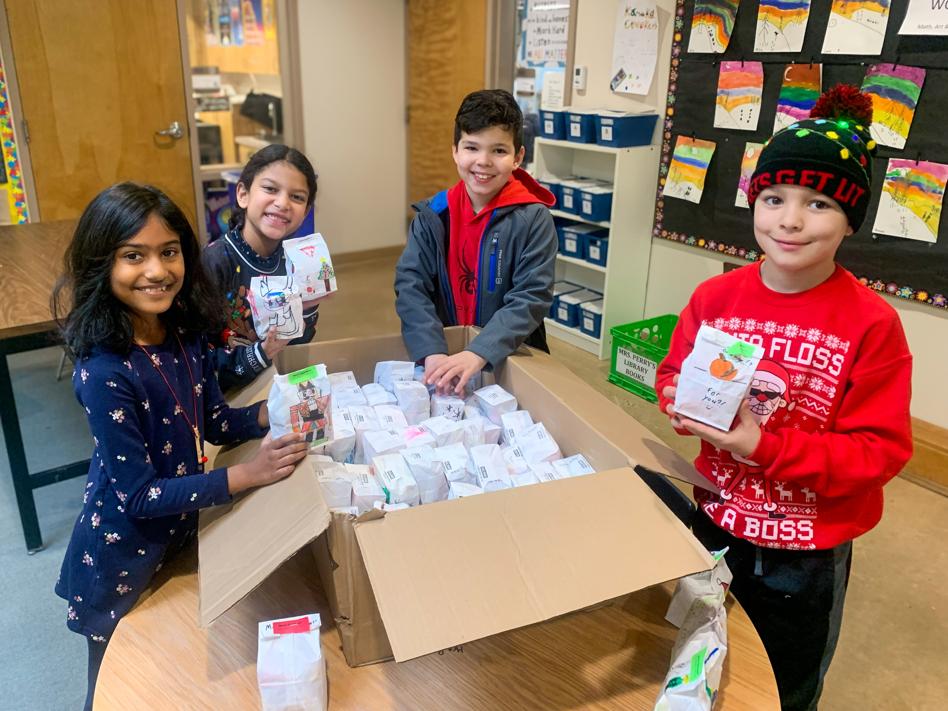 Kanaka Creek students place decorated holiday treat bags into a box.